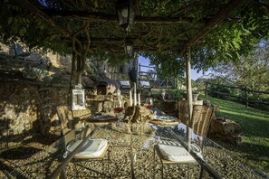Un espace extérieur aménagé pour les repas, avec des tables et des chaises, une pergola et un mur de pierre en arrière-plan.