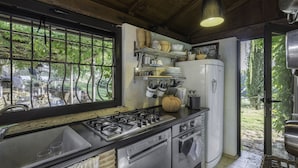 Eine Küche mit Gasherd, Geschirrspüler und Kühlschrank. Ein Fenster bietet Blick auf Bäume, und eine Tür führt nach draußen.