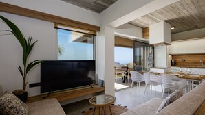 A modern living room with a flat-screen TV, a large plant, and a dining area with white chairs and a wooden table. - Seaview villa w/private pool, 4km to Plakias beach (Mariou)