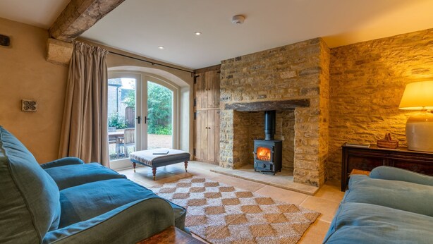 A cozy living room with a stone fireplace, a sofa, and a view through a glass door to an outdoor area. - The Coach House - sleeps 4 guests  in 2 bedrooms (Cold Aston)