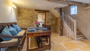 A dining area with a wooden table set for four, a stone wall, and a staircase. - The Coach House - sleeps 4 guests  in 2 bedrooms (Cold Aston)