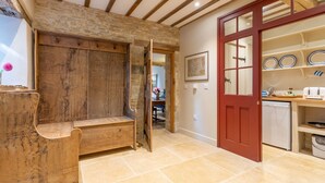 A rustic kitchen with a wooden bench, a red door, and a tiled floor. - The Coach House - sleeps 4 guests  in 2 bedrooms (Cold Aston)