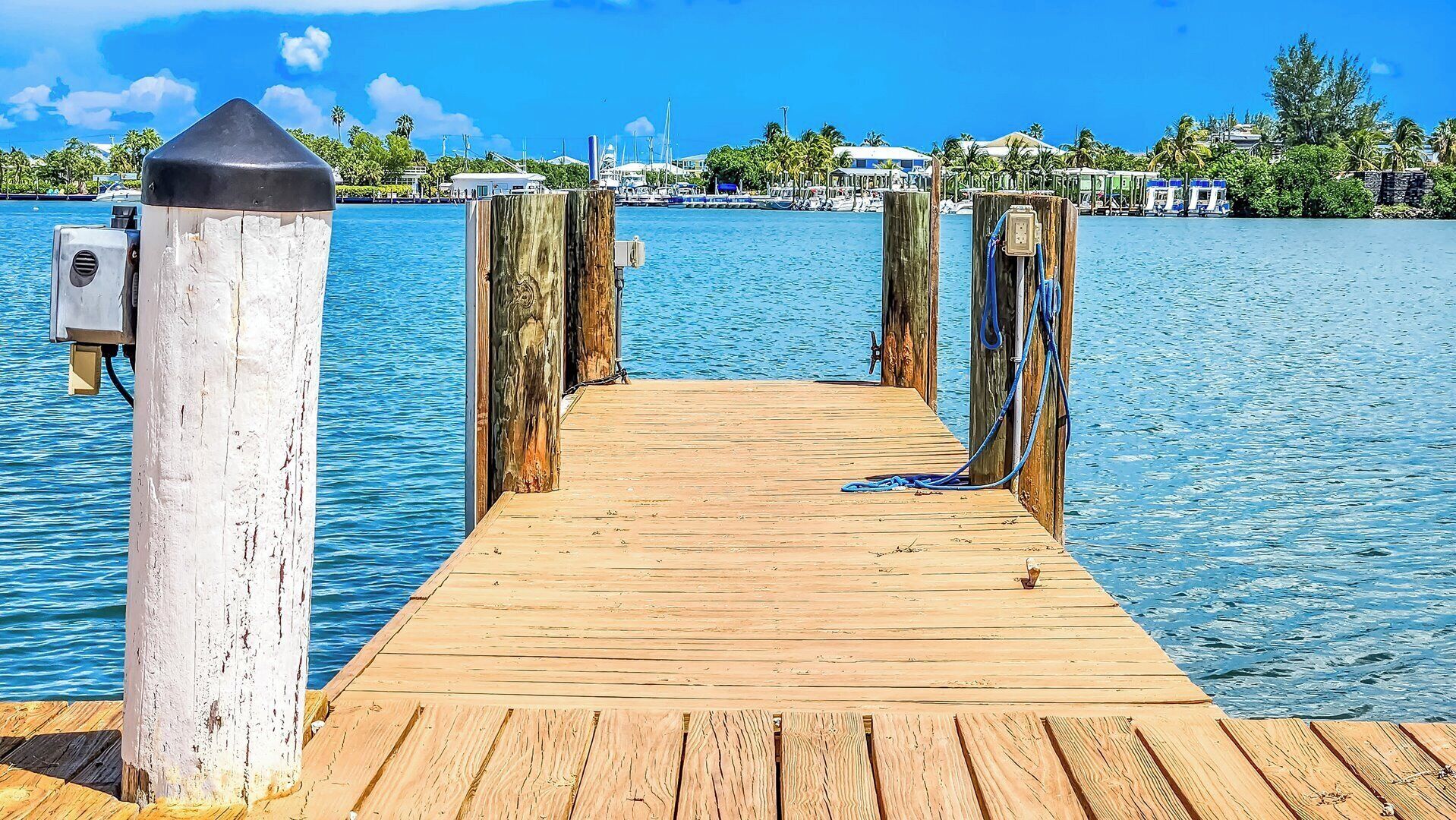 A wooden pier leading into calm waters, with a clear sky and distant buildings.