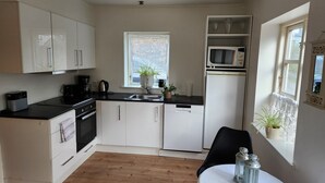 A compact kitchen with white cabinets, a black countertop, a microwave, a sink, and a window with a view. - Breakaway Cottage (Grasten)