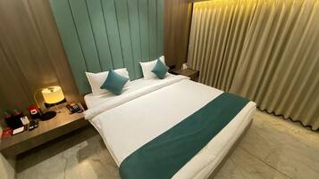 Habitación de hotel con una cama grande, una mesita de noche con una lámpara, un teléfono y una pequeña mesa con un libro y una botella.