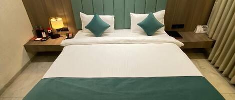 A hotel room with a large bed, two pillows, a bedside table with a lamp, and a nightstand with a phone and other items.