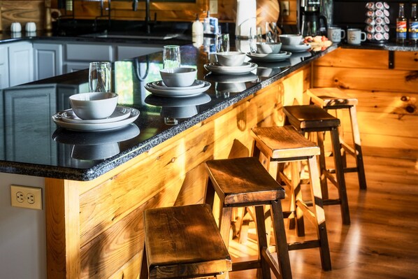 A kitchen with a wooden island, bar stools, and a countertop with dishes and glasses. - Fire Pit*2 Hot Tubs*Basketball*Game Room*Mtn Views (Sevierville)