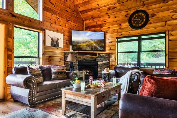 Ein gemütliches Blockhaus-Interieur mit Kamin, Ledersofas, einem Holztisch und einem großen Fernseher.