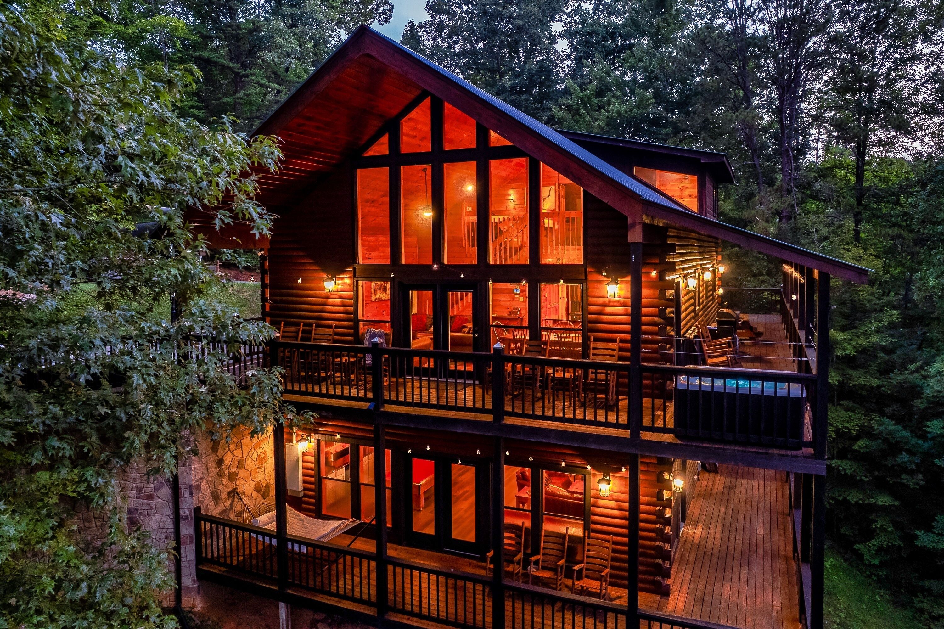 A two-story log cabin with multiple windows and a balcony, surrounded by trees.