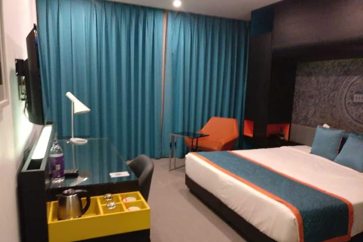 A hotel room with a bed, a desk with a lamp, a chair, and a minibar.