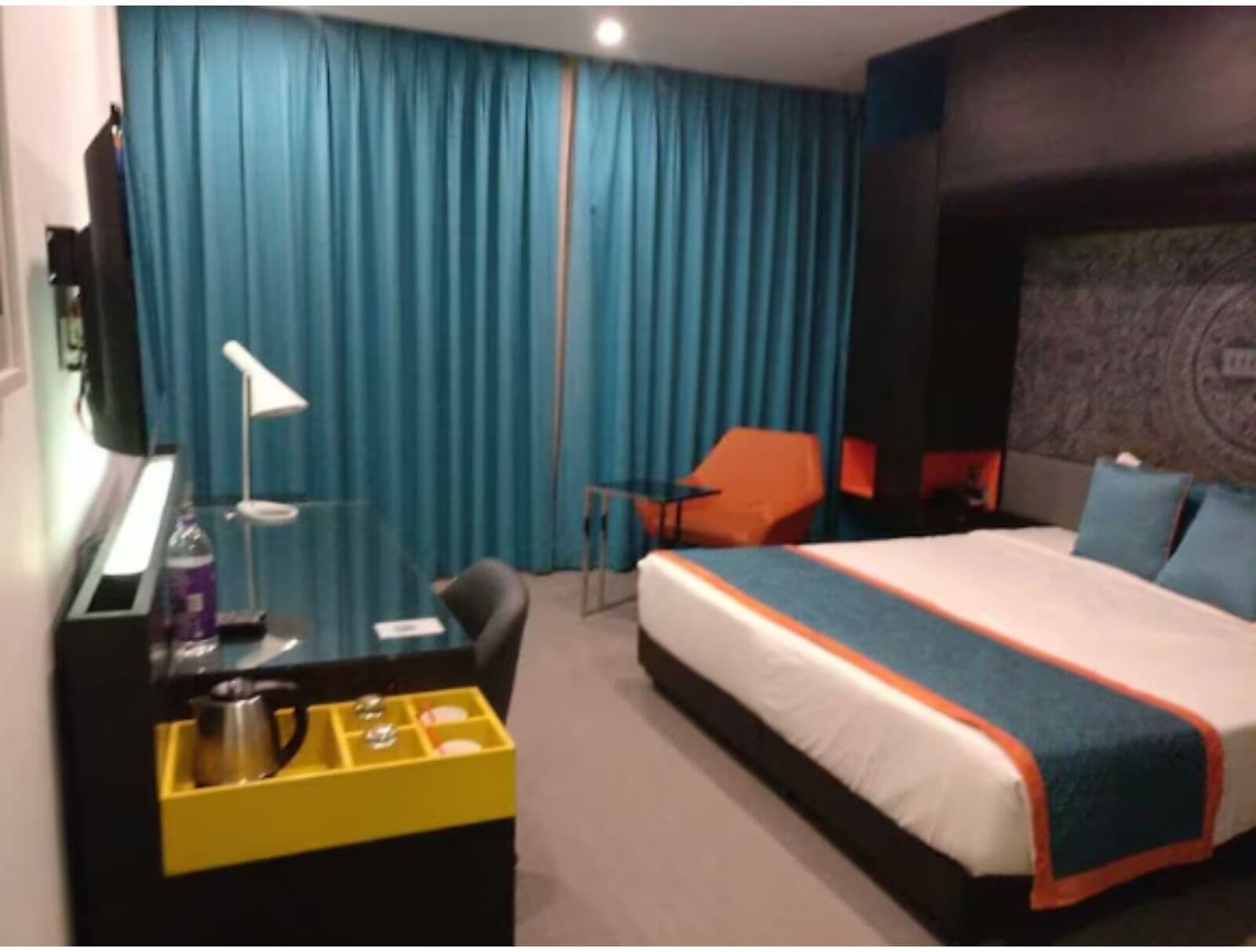 Et hotelværelse med en seng, et skrivebord med lampe, en stol og et minikøleskab.
