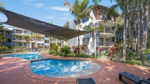 Un espace piscine d’hôtel comprenant un jacuzzi, des chaises longues et une terrasse couverte.