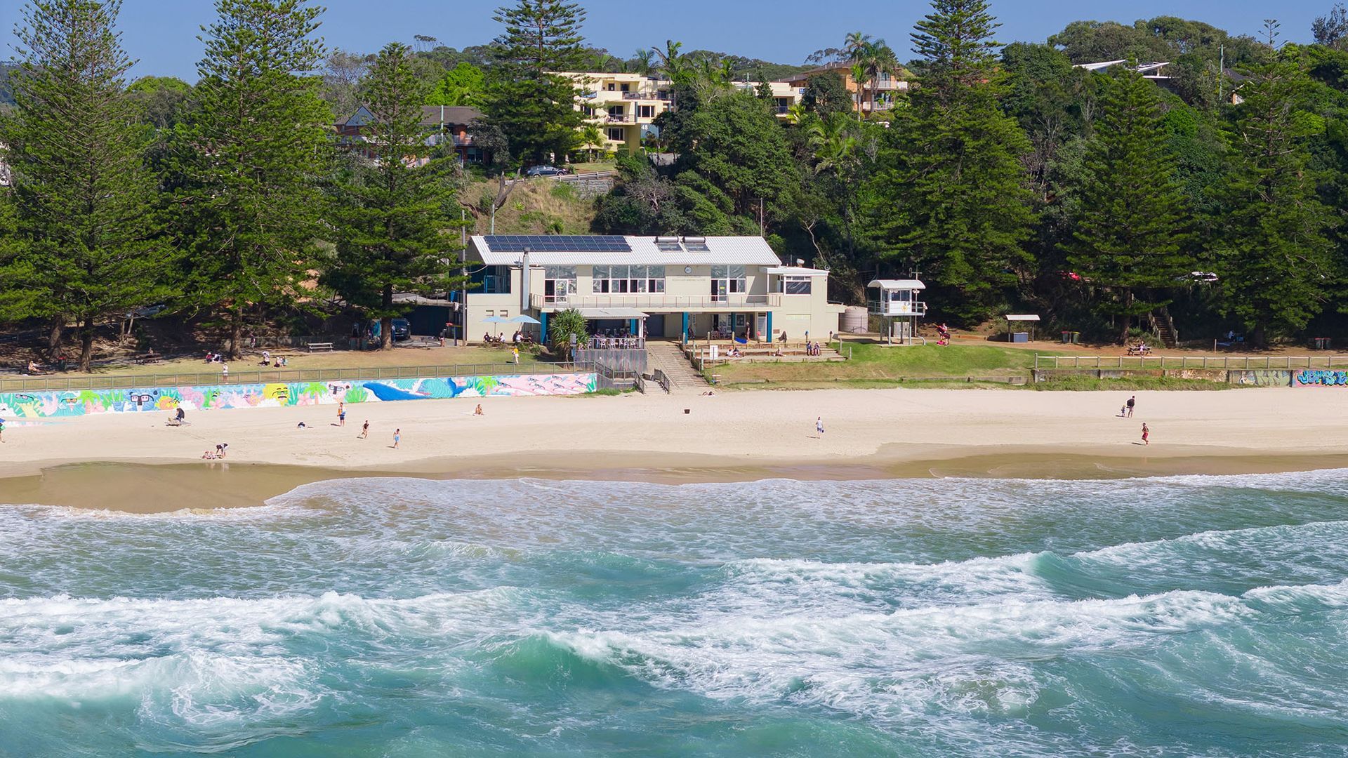 A beach with a building that has a flat roof and a swimming pool.