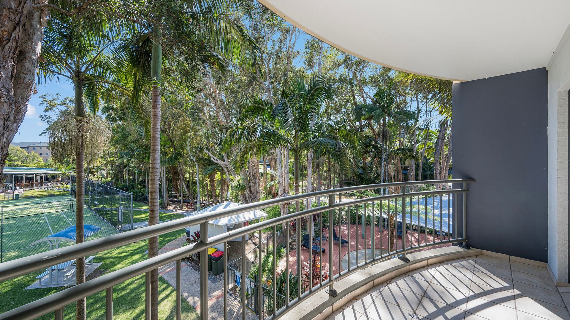 A balcony with a view of a tennis court and surrounding trees.