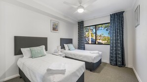 Une chambre d’hôtel avec deux lits, un ventilateur de plafond, une fenêtre avec des rideaux et un tableau encadré au mur.