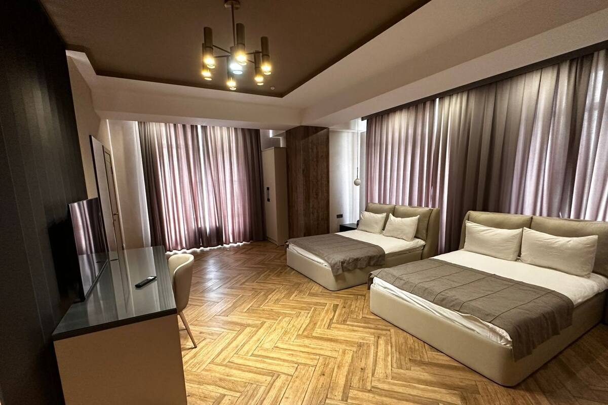 A modern bedroom with a wooden herringbone floor, a large bed, a sofa bed, a desk, and a TV.
