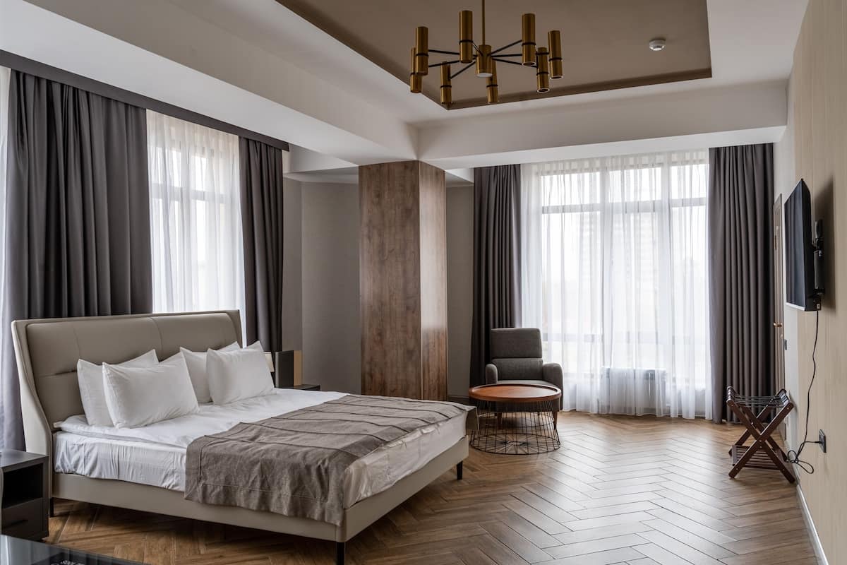 A modern hotel room with a large bed, a round coffee table, a chair, and a TV mounted on the wall.