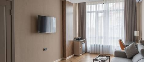 Una sala moderna con un televisor de pantalla plana montado en la pared, un juego de sofá, una mesita y una ventana con cortinas traslúcidas.