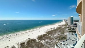 A beach with a clear view of the ocean, a sandy shore, and a high-rise building with a curved balcony. - Beachfront 4BR Corner Unit!  Lazy River and Water Slide!! (Orange Beach)