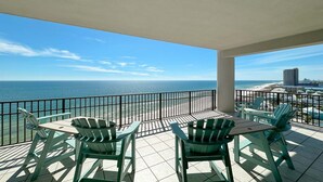 A balcony with a view of the ocean and beach, featuring a table and chairs.