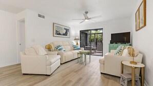 A spacious living room with a white sofa set, a small table, and a ceiling fan. - Beachside Gem!  Sea Woods Condo 153 - Close to Pool & Beach Access (New Smyrna Beach)