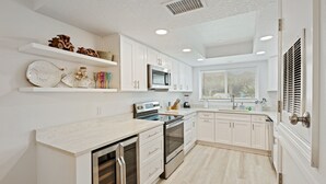 A modern kitchen with white cabinetry, stainless steel appliances, and a light wood floor. - Beachside Gem!  Sea Woods Condo 153 - Close to Pool & Beach Access (New Smyrna Beach)