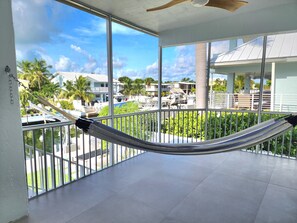 A balcony with a hammock, large windows, and a view of a resort area with buildings and palm trees. - Best Canal in the Keys! 4/3 Waterfront,Heated Pool, Ocean access, Dock, 5⭐ Rated (Tavernier)