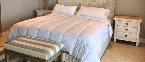 A bedroom with a large bed, a bench, a nightstand, a lamp, and a ceiling fan.