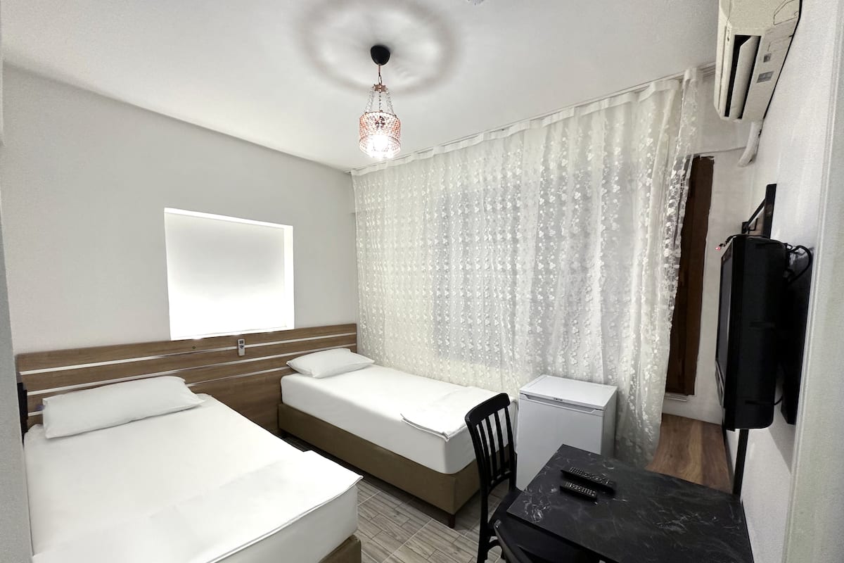 A hotel room with two beds, a desk, a chair, a TV, an air conditioner, and a decorative light fixture.