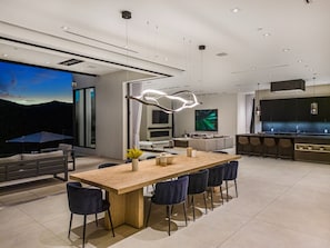 A modern kitchen with a central island, bar seating, and a large TV screen.