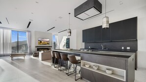 A modern kitchen with a central island, bar stools, and a large TV.