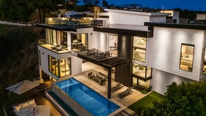 A modern house with a large swimming pool, outdoor seating, and a well-lit patio area.