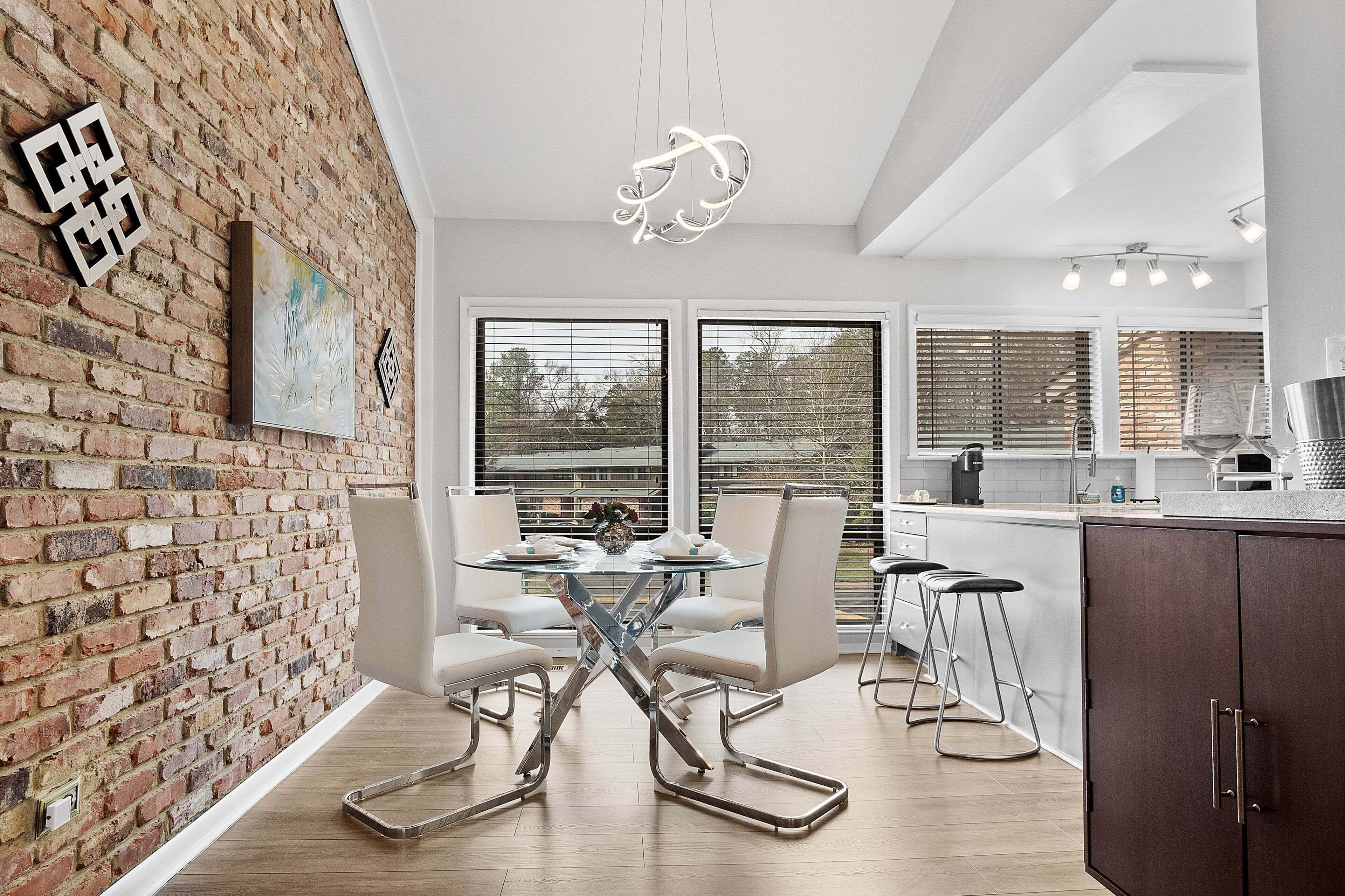 A modern kitchen with a brick wall, a glass dining table, and bar stools.