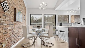 A modern kitchen with a brick wall, a glass dining table, and bar stools. - Only two miles to UNC campus (Chapel Hill)