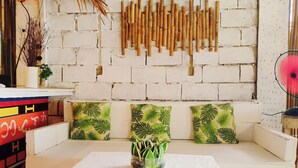 Ein weißes Sofa mit grünen Kissen im Palmenblatt-Design, ein weißer Couchtisch und eine Wand, verziert mit Bambusstäben und einem Fächer.