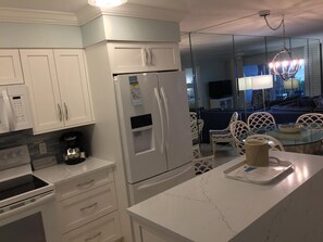 Una cocina moderna con armarios blancos, un refrigerador empotrado, una cafetera y una mesa de comedor de vidrio con sillas.