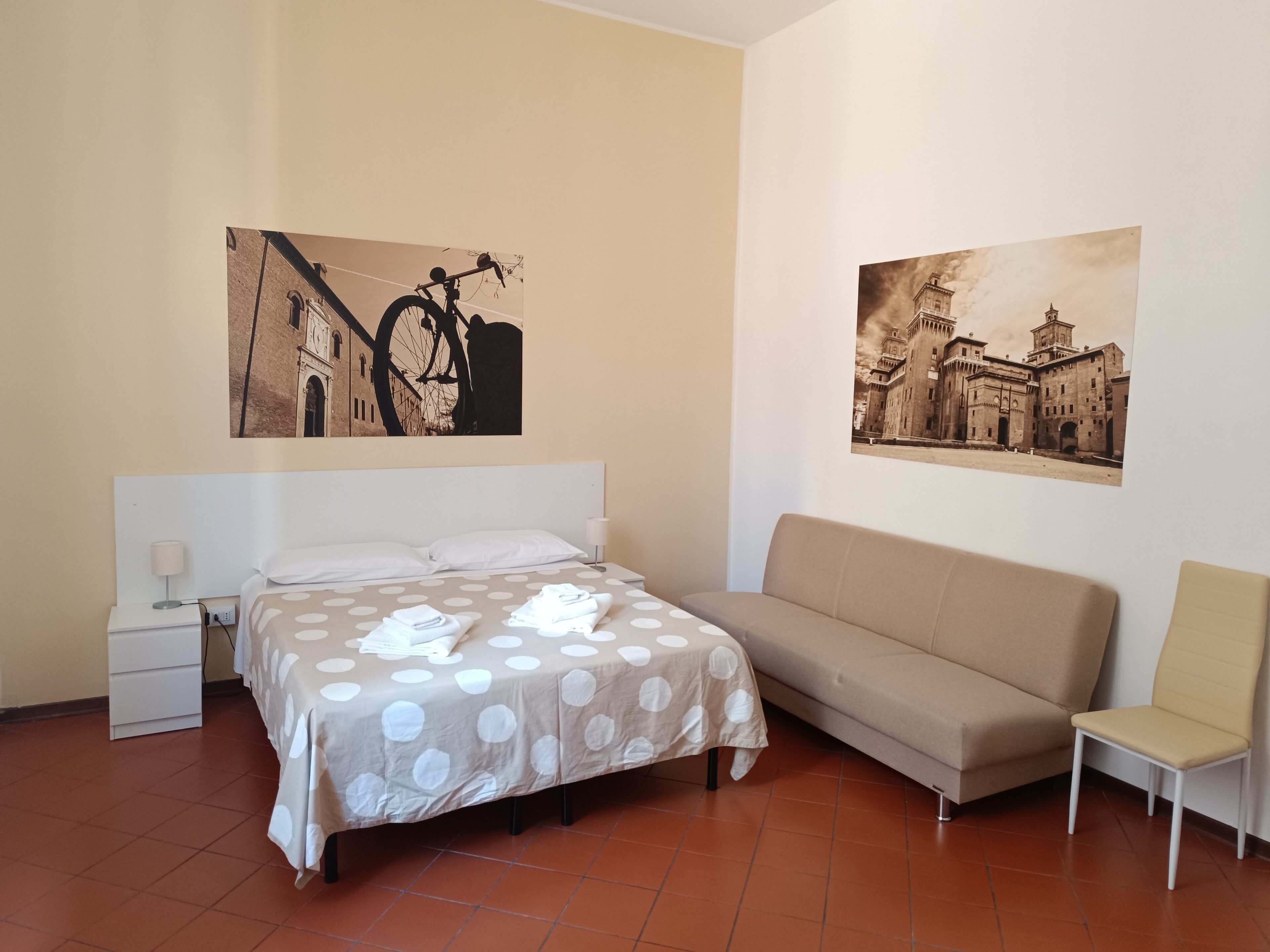 A hotel room with a bed, a sofa, a chair, and two wall-mounted pictures.