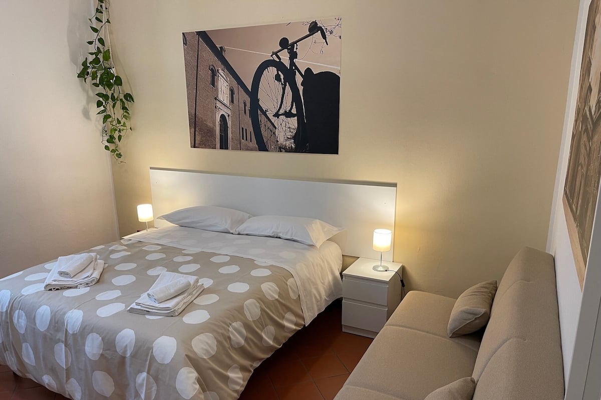 A neatly made bed with a polka dot bedspread, a bedside table with a lamp, and a sofa.