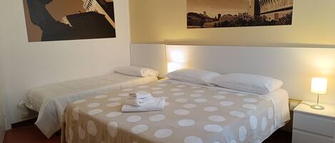 Habitación de hotel con dos camas, una mesita de noche y una lámpara de pared.