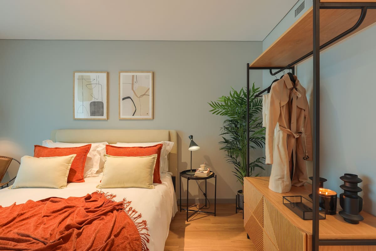 Un dormitorio moderno con cama, mesita de noche, lámpara y espejo con bata colgada.