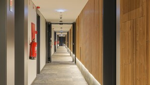 A long, narrow hallway with a fire extinguisher on the left, a wooden panel wall on the right, and a carpeted floor. - Nôma Living Icon Apartments (Porto)
