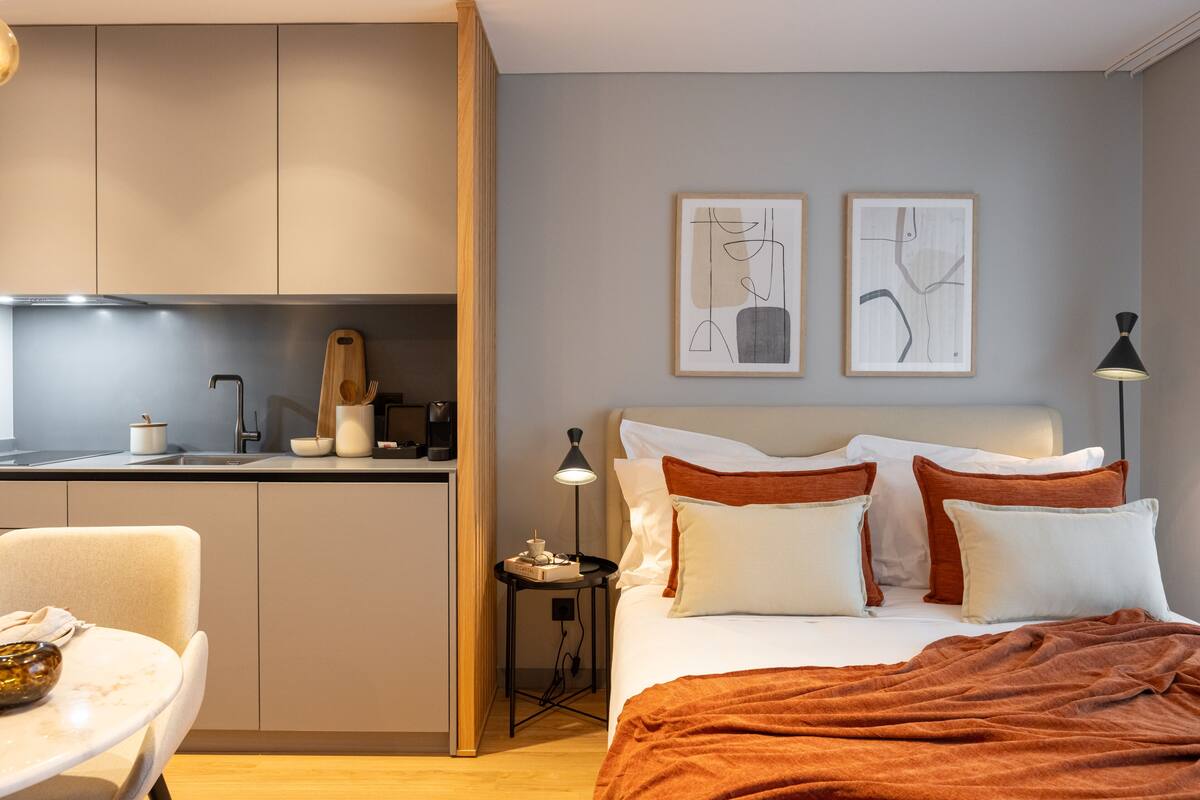 Una habitación de hotel moderna con cama, mesita de noche y una pequeña kitchenette.