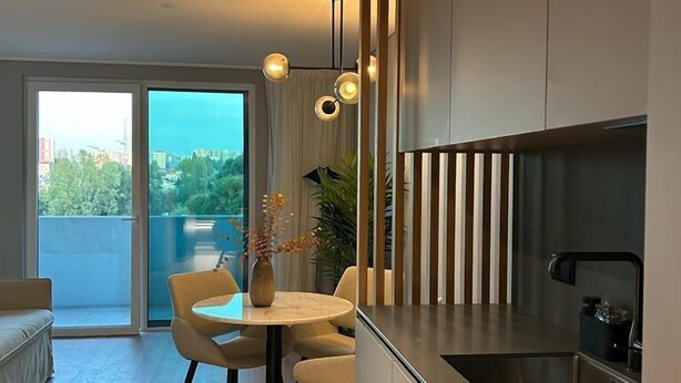 A modern kitchen with a built-in stove, a dining area with a table and chairs, and a view of the outdoors through a sliding door. - Nôma Living Icon Apartments (Porto)