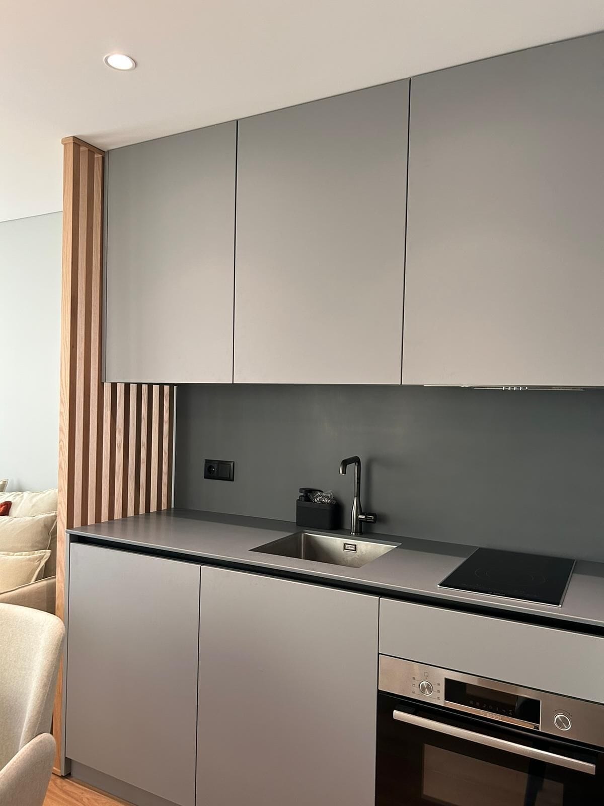 A modern kitchen with grey cabinets, a black countertop, a built-in oven, and a sink.
