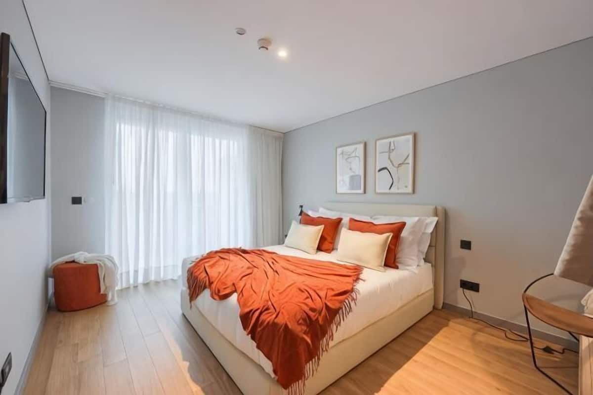 Un dormitorio con cama, una silla, un escritorio y una ventana con cortinas.