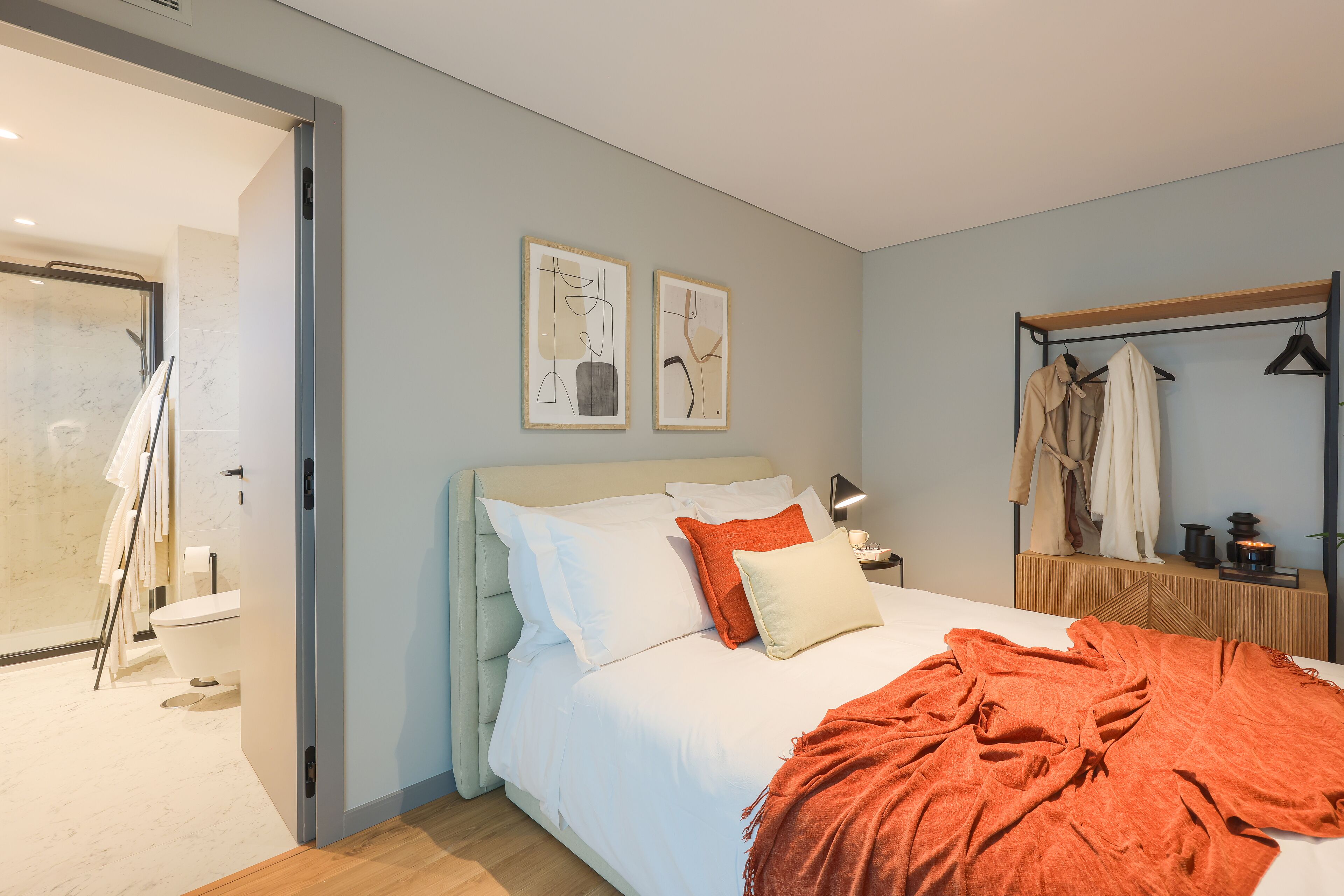 Une chambre à coucher moderne avec un lit, une table de chevet, un miroir et un portant à vêtements.