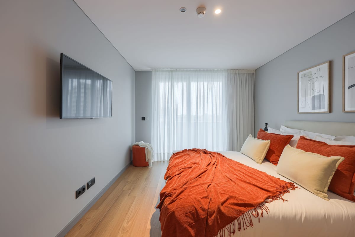 Un dormitorio moderno con cama, televisor y ventana con cortinas.
