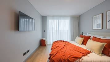 A modern bedroom with a bed, a television, and a window with curtains.