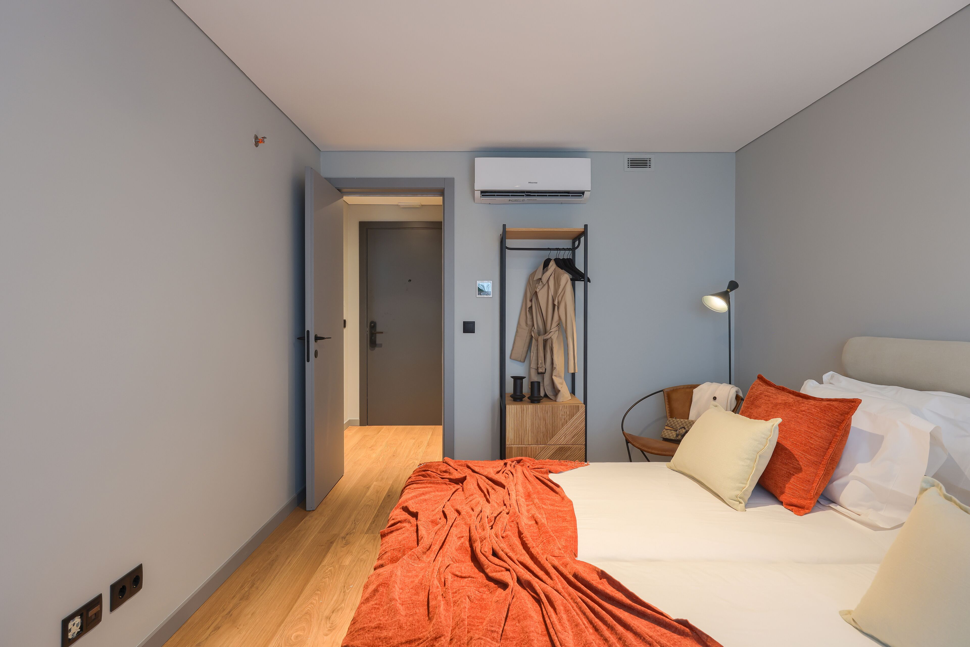 A bedroom with a bed, a bedside table, a lamp, a wardrobe, and an air conditioning unit.