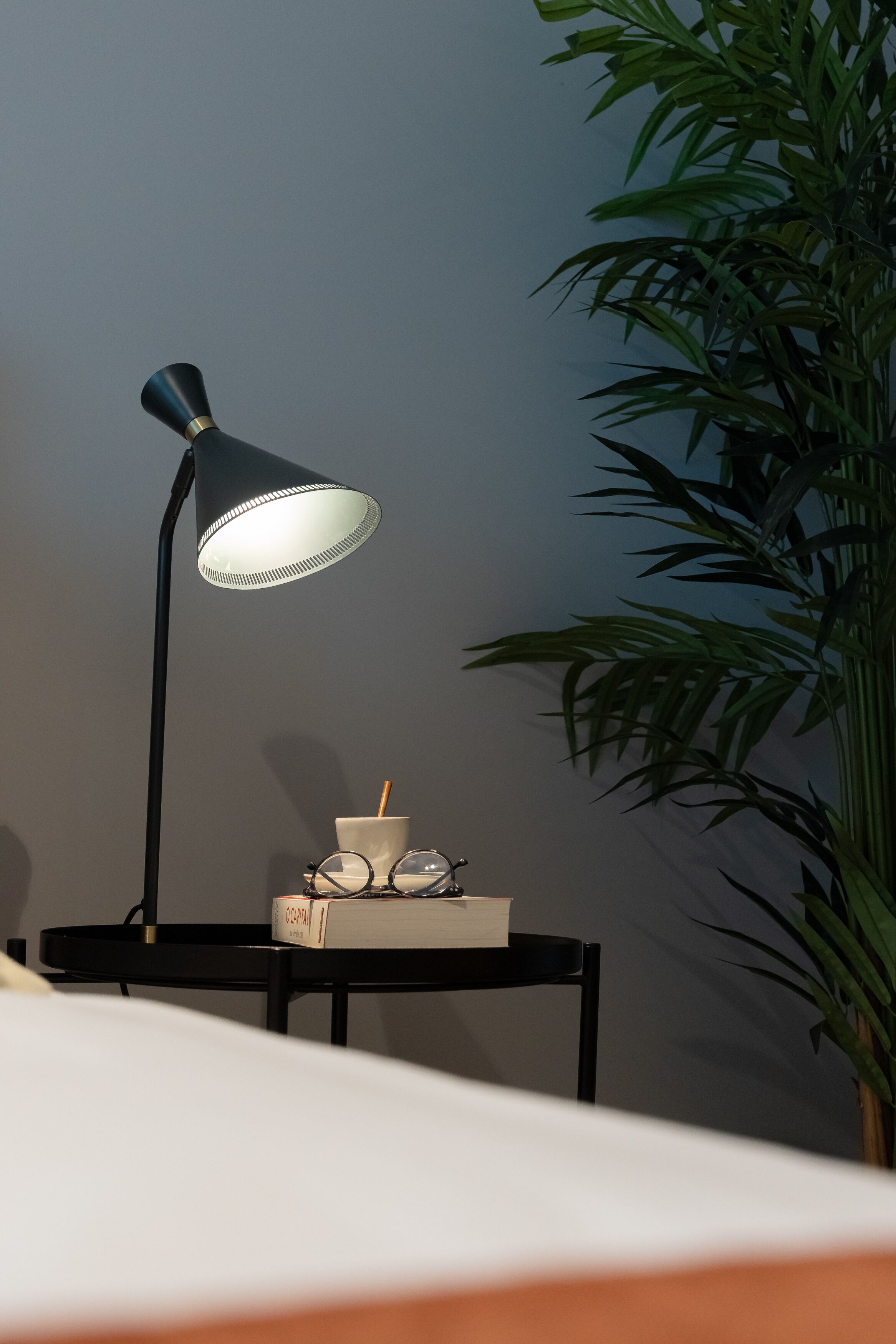 Une table de chevet avec une lampe, des lunettes, une tasse et un livre.